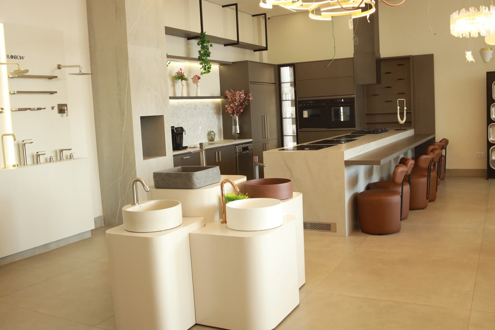 Ambiente de cozinha montado no showroom da KMAC, com cubas, bancada em pedra e iluminação pendente